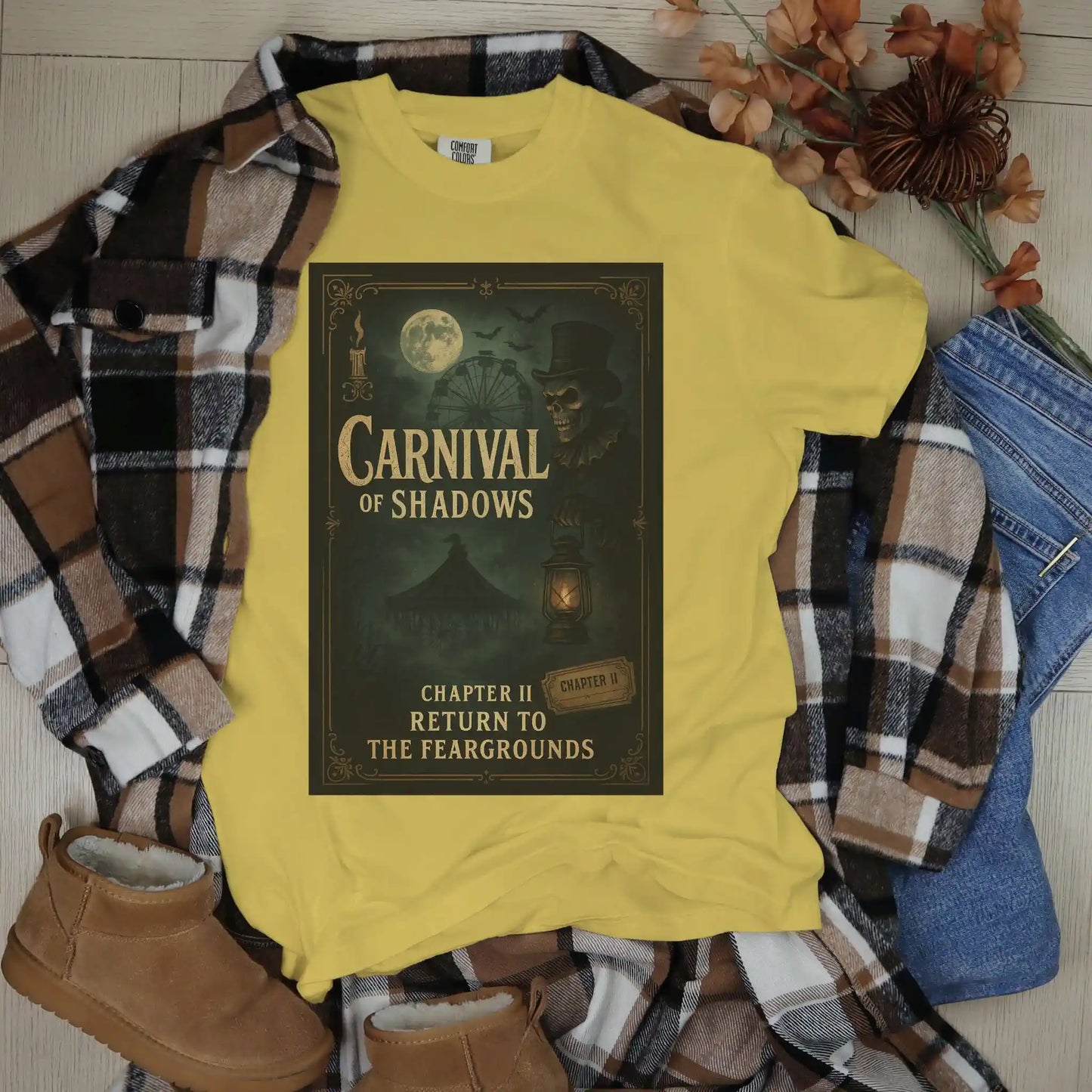 Yellow t-shirt with 'Carnival of Shadows' design on a plaid shirt and jeans background