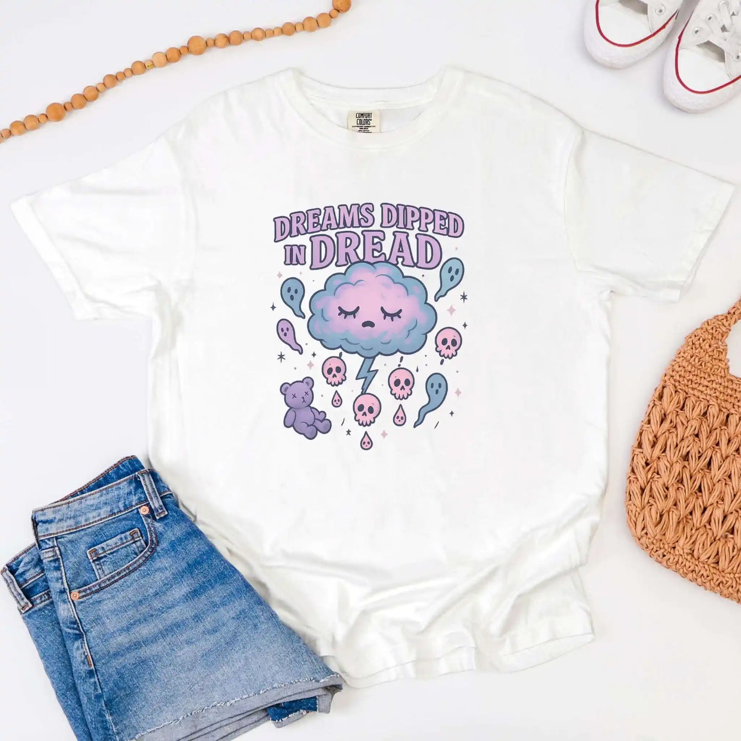 White t-shirt with a "Dreams Dipped in Dread" graphic design, featuring a cloud, teddy bear, and text on a white background.