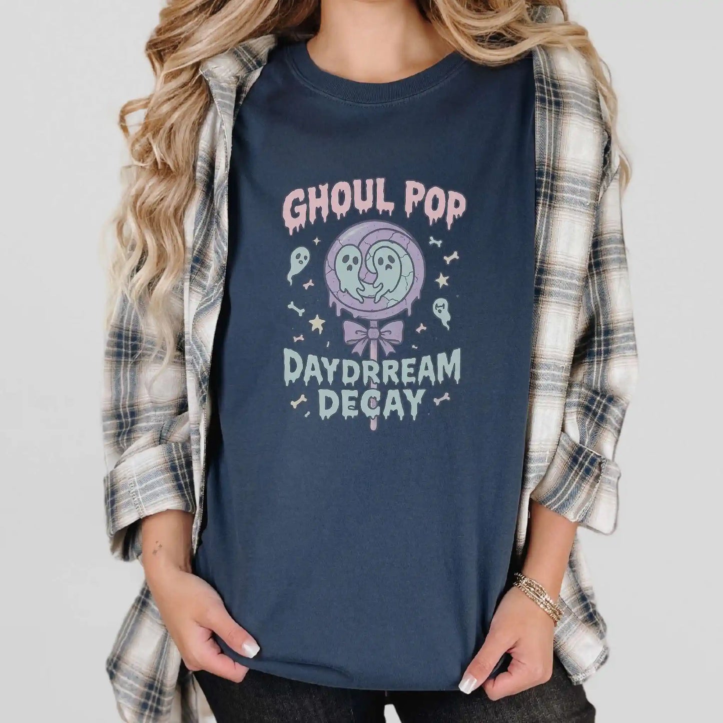 Person wearing a navy blue t-shirt with 'Ghoul Pop Daydream Decay' design, plaid shirt over it, standing in front of a white background.