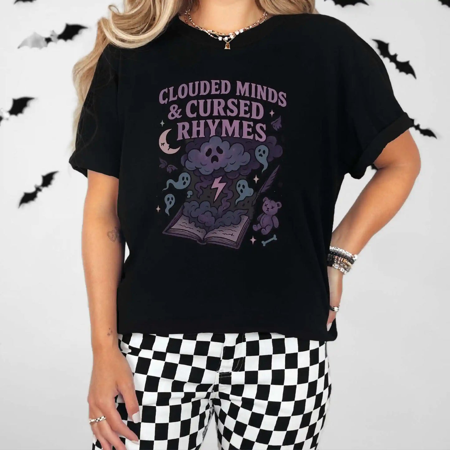 Person wearing a black t-shirt with "clouded minds & cursed rhymes" graphic design and text, checkered leggings in front of a Halloween-themed background.