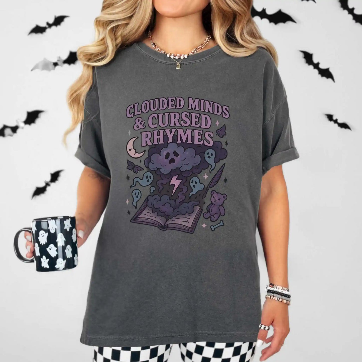 Person wearing a dark gray t-shirt with a "clouded minds & cursed rhymes" graphic design and text, holding a mug with a ghost pattern.