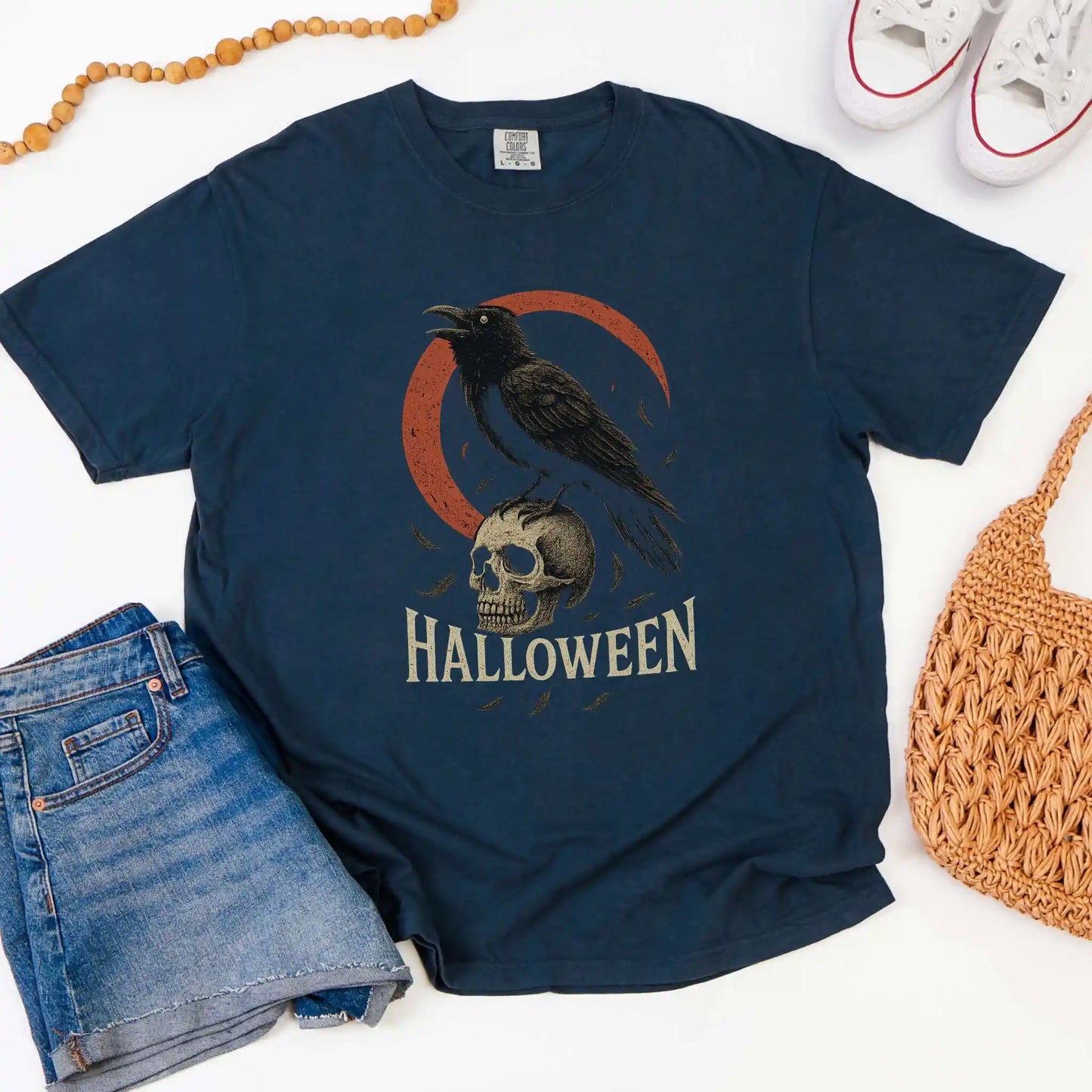 Navy blue t-shirt with Halloween design featuring a crow and skull, displayed with jeans, shoes, and a bag.