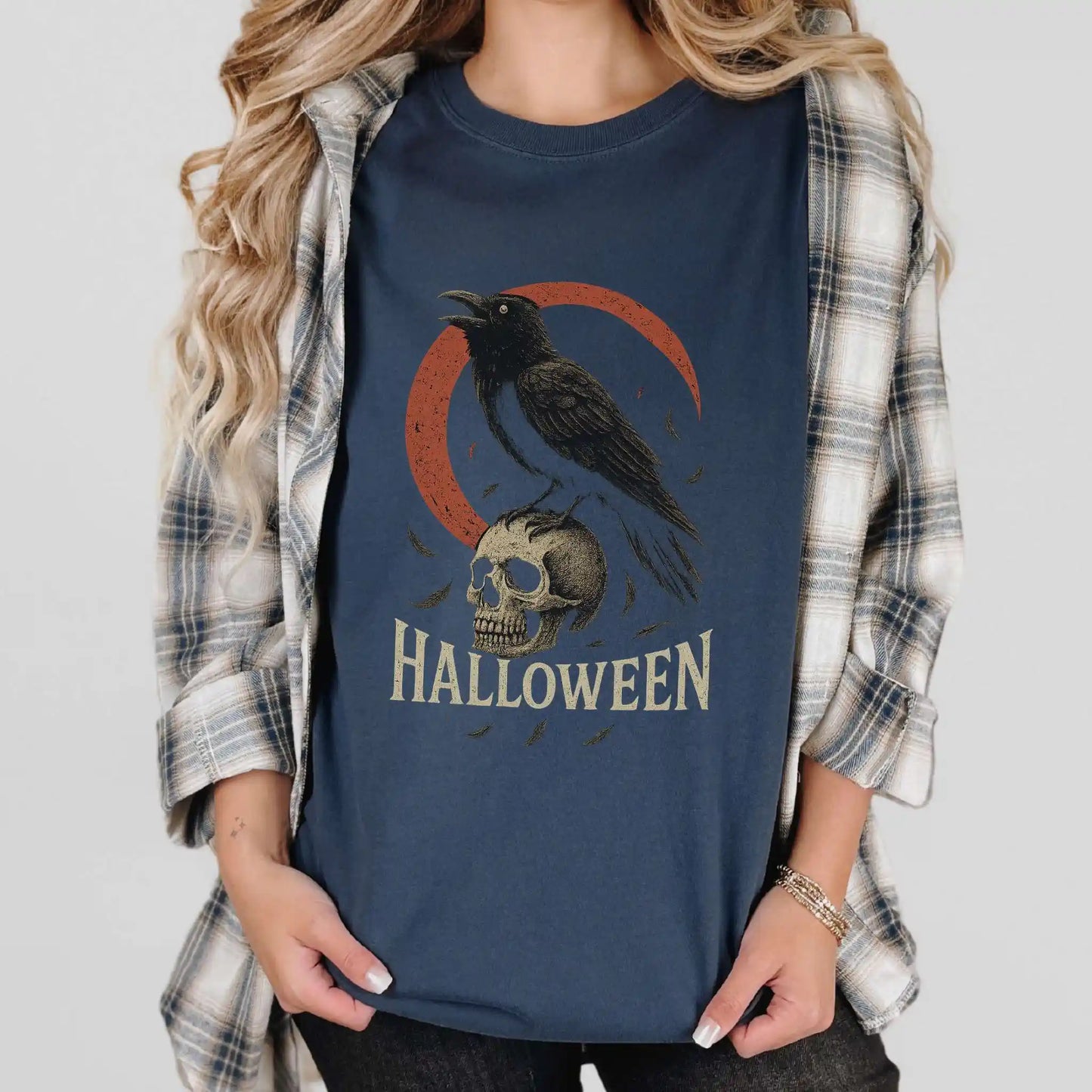 Person wearing a navy blue t-shirt with a Halloween design featuring a skull and crow, paired with a plaid shirt.