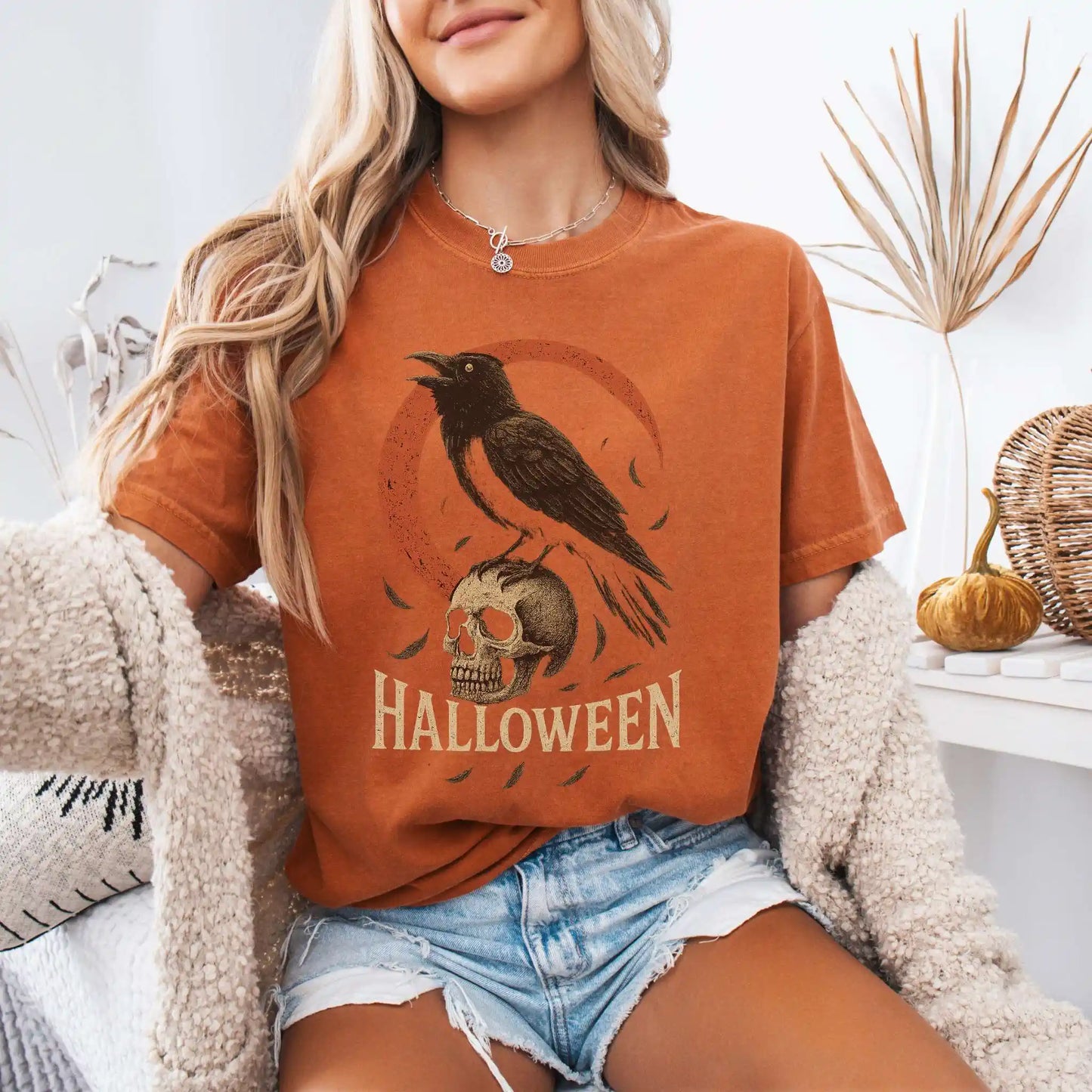 Person wearing an orange Halloween-themed t-shirt with a crow and skull design.