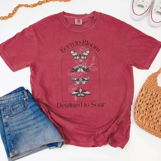 Red t-shirt with butterfly design and 'Born to Bloom, Destined to Soar' text, paired with jeans and a bag on a white background