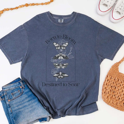 Blue t-shirt with butterfly design and 'Born to Bloom, Destined to Soar' text, paired with jeans and a bag on a white background