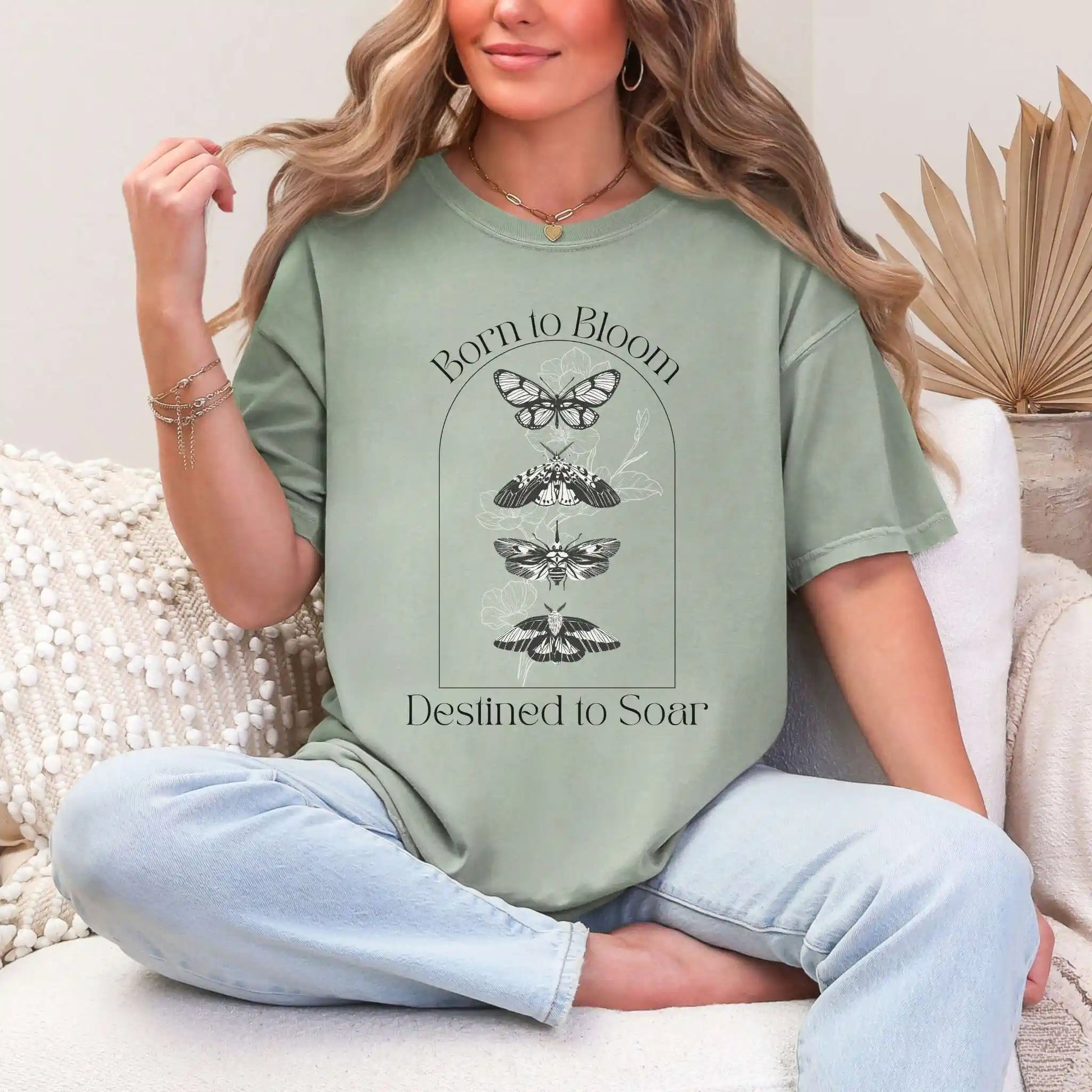 Woman wearing a green t-shirt with butterfly design and 'Born to Bloom, Destined to Soar' text, sitting on a couch.