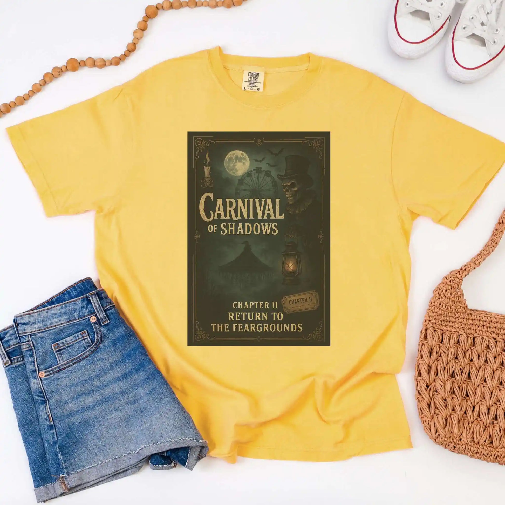 Yellow t-shirt with 'Carnival of Shadows' design, paired with denim shorts and a woven bag on a white background.