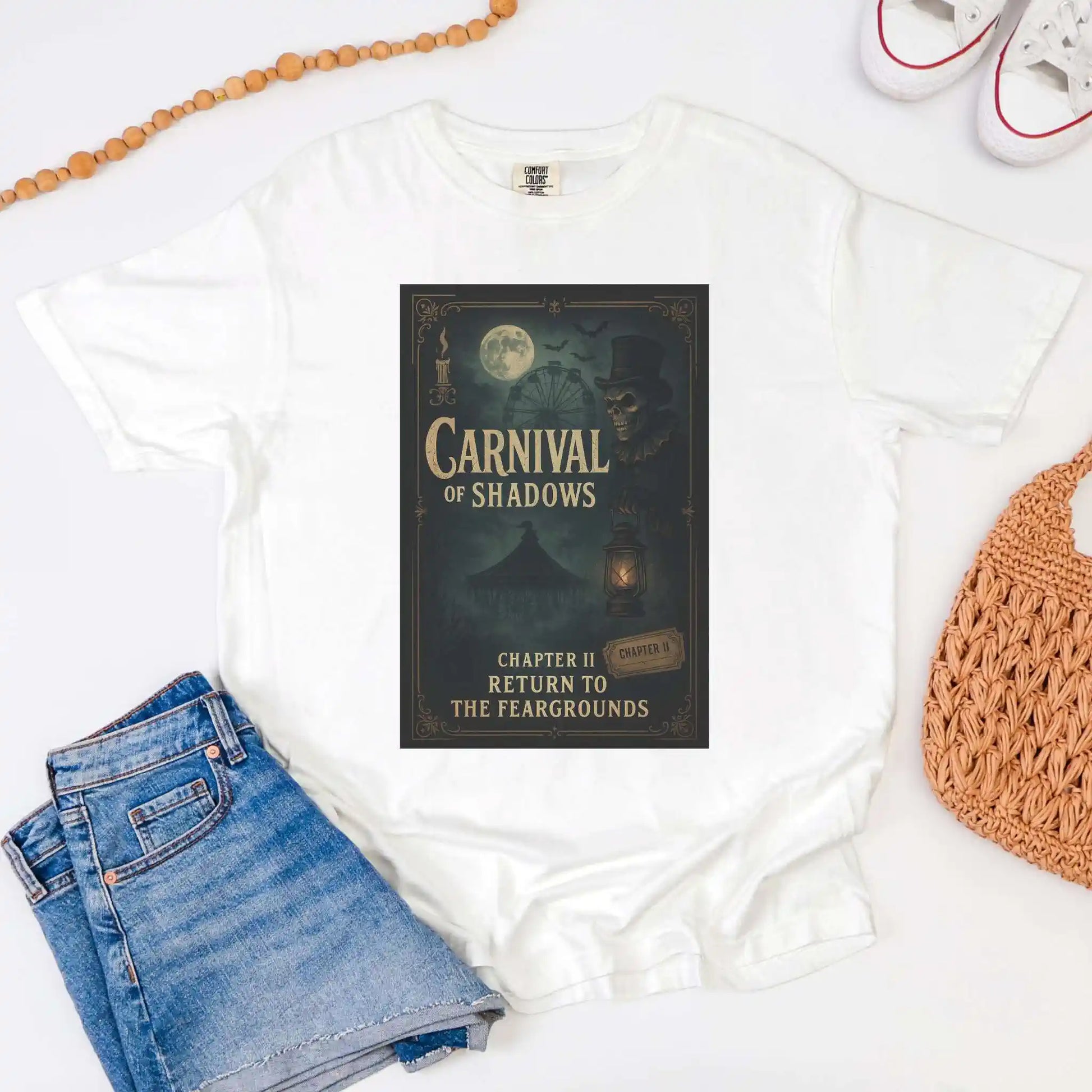 White t-shirt with 'Carnival of Shadows' book cover, blue jeans, and a woven bag on a white background