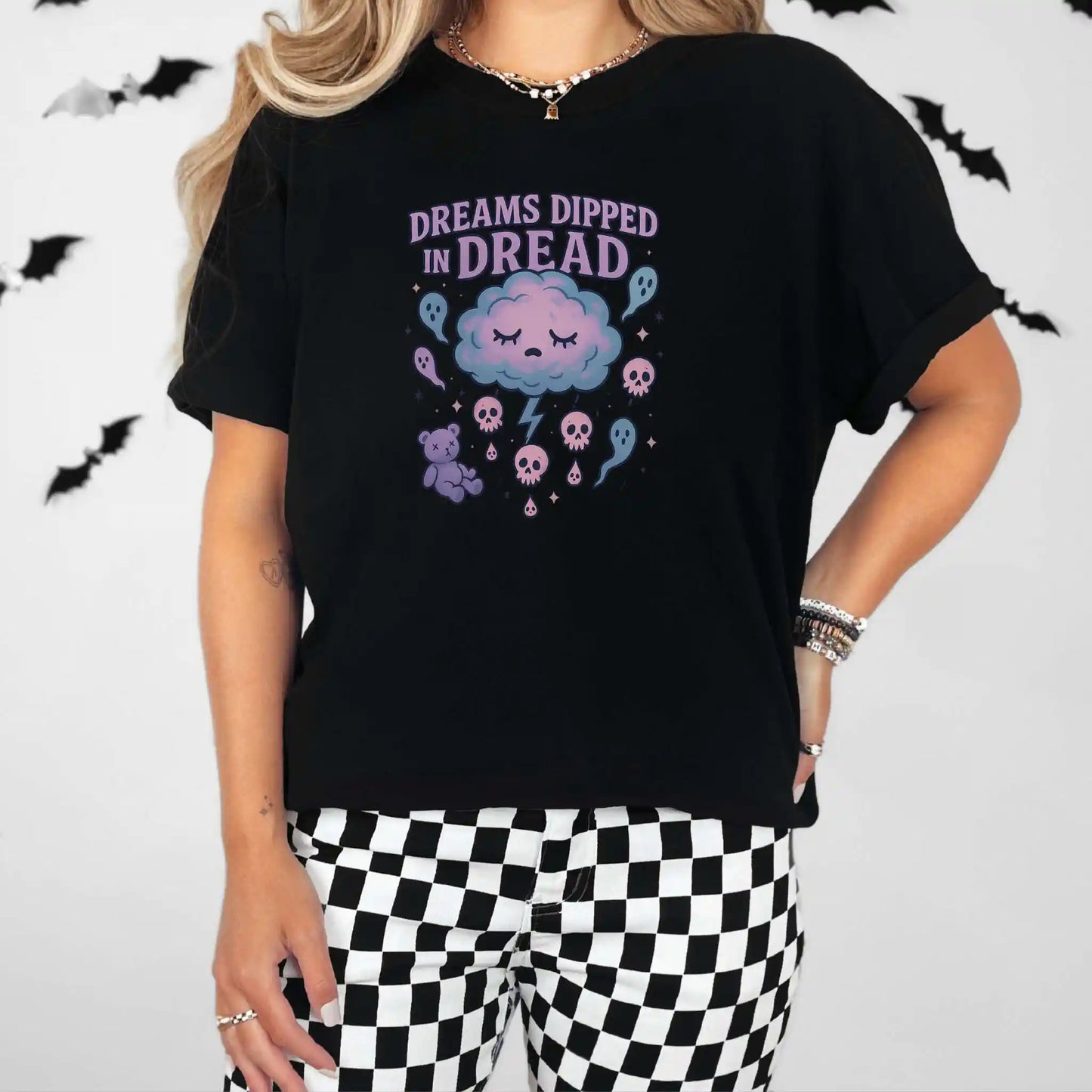 Person wearing a black t-shirt with a "Dreams Dipped in Dread" graphic design with clouds and ghosts, standing against a plain background with bats.