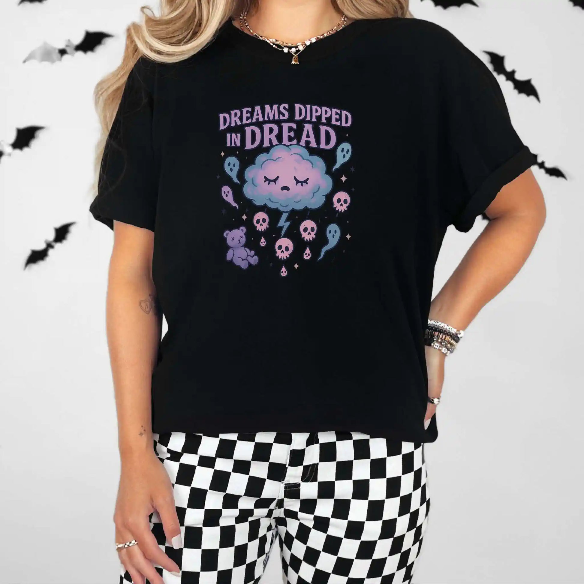 Person wearing a black t-shirt with a "Dreams Dipped in Dread" graphic design with clouds and ghosts, standing against a plain background with bats.
