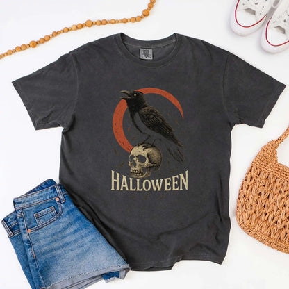 Black t-shirt with Halloween design featuring a crow and skull, displayed with jeans and a bag.