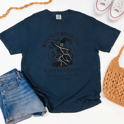 Navy blue t-shirt with 'Witches Brew Co. Coffee House' design on a white background with jeans and a bag.