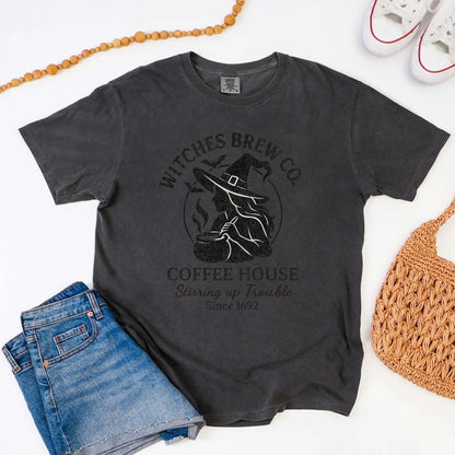 Dark gray t-shirt with 'Witches Brew Co. Coffee House' design on a white background with jeans and a bag.