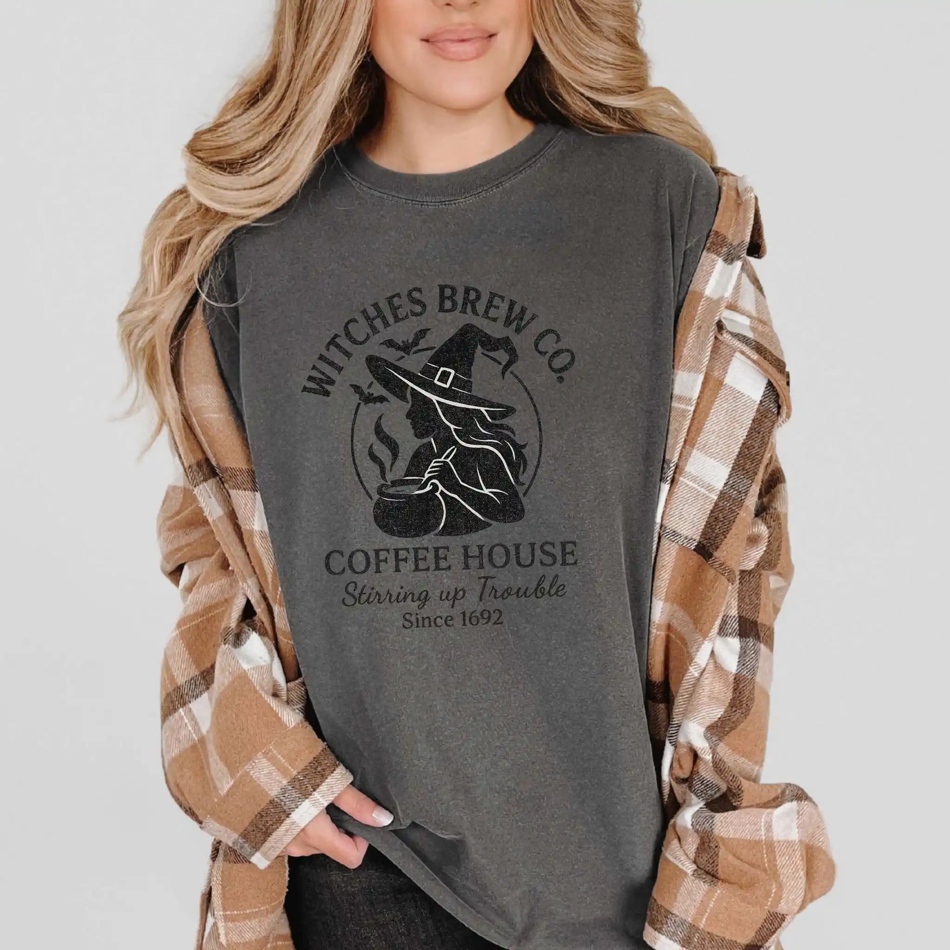 Person wearing a gray t-shirt with 'Witches Brew Co. Coffee House' design, flanked by a plaid shirt.