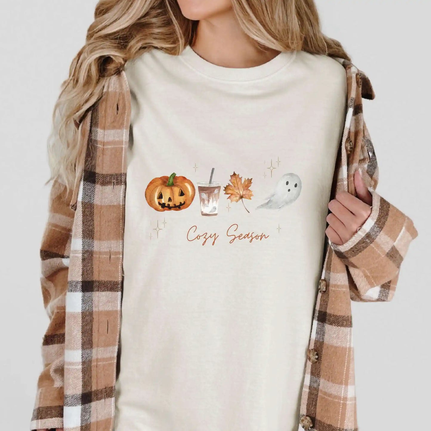 Person wearing a ivory tshirt with autumn-themed graphics and 'Cozy Season' text, paired with a plaid shirt.