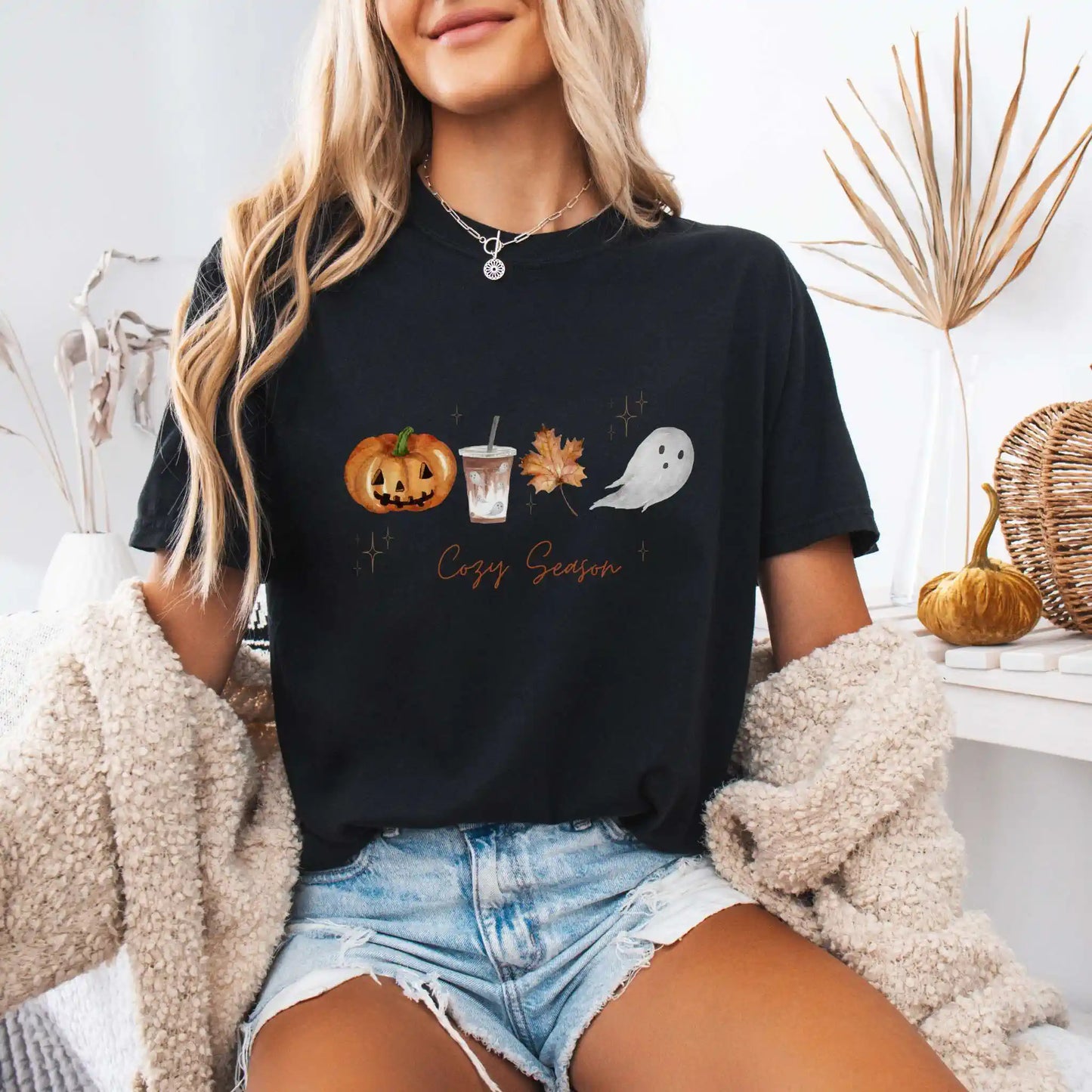 Person wearing a black t-shirt with Halloween-themed graphics and 'Cozy Season' text, sitting indoors.