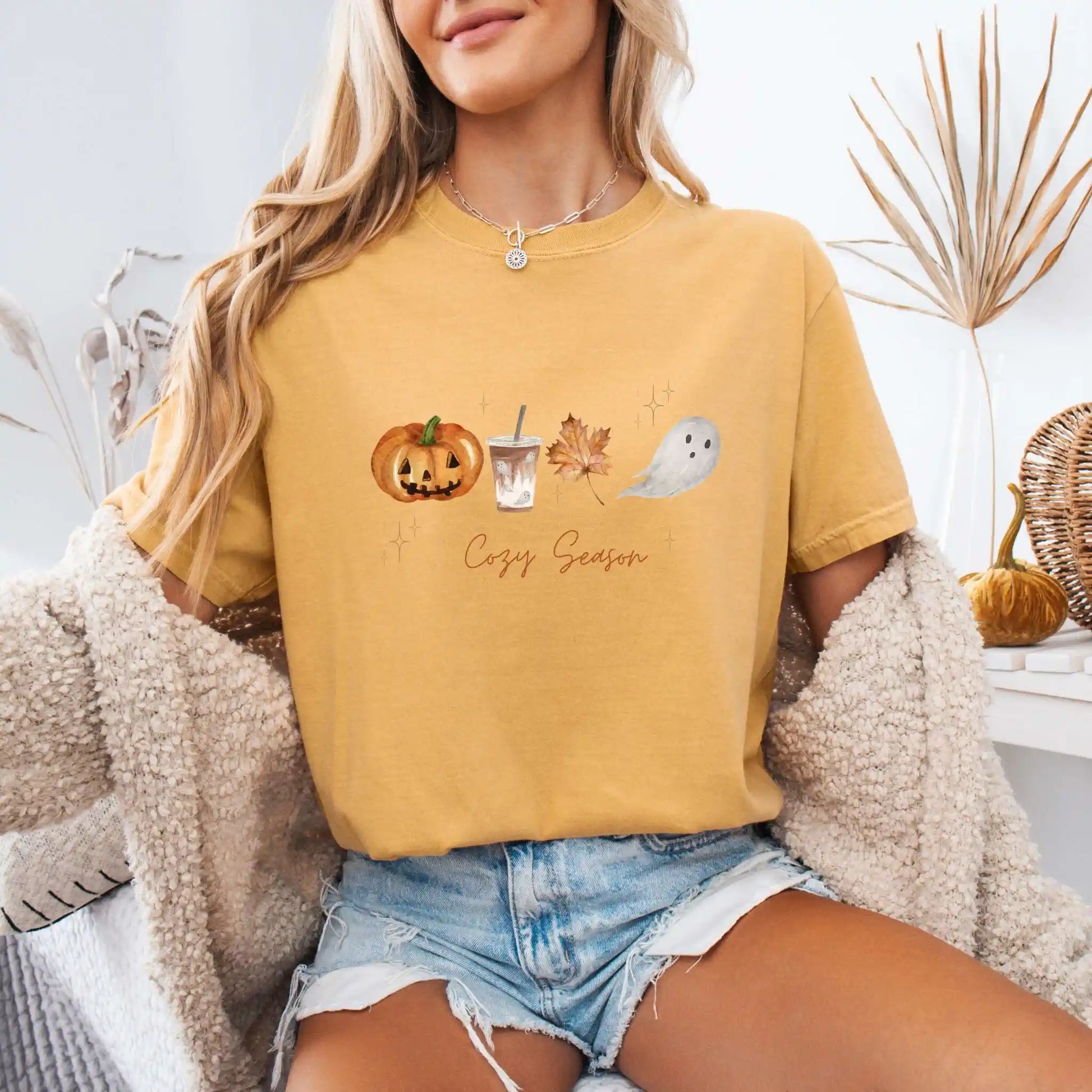 Person wearing a mustard yellow t-shirt with Halloween-themed graphics and 'Cozy Season' text, sitting indoors.