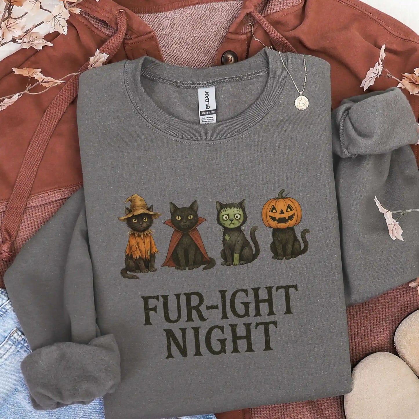 Charcoal sweatshirt with Halloween-themed design featuring cats in costumes and 'Fur-ight Night' text, lying on a brown jacket background.