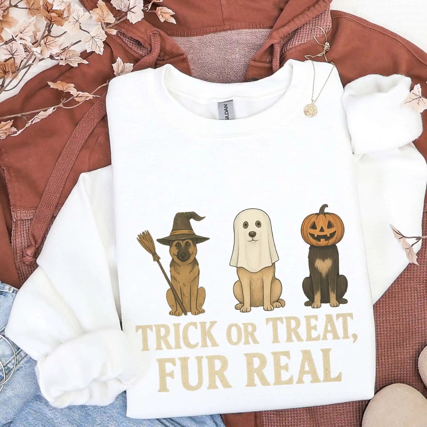 White sweatshirt with Halloween-themed dog illustrations and "Trick or treat fur real" text on a brown jacket and jeans background.