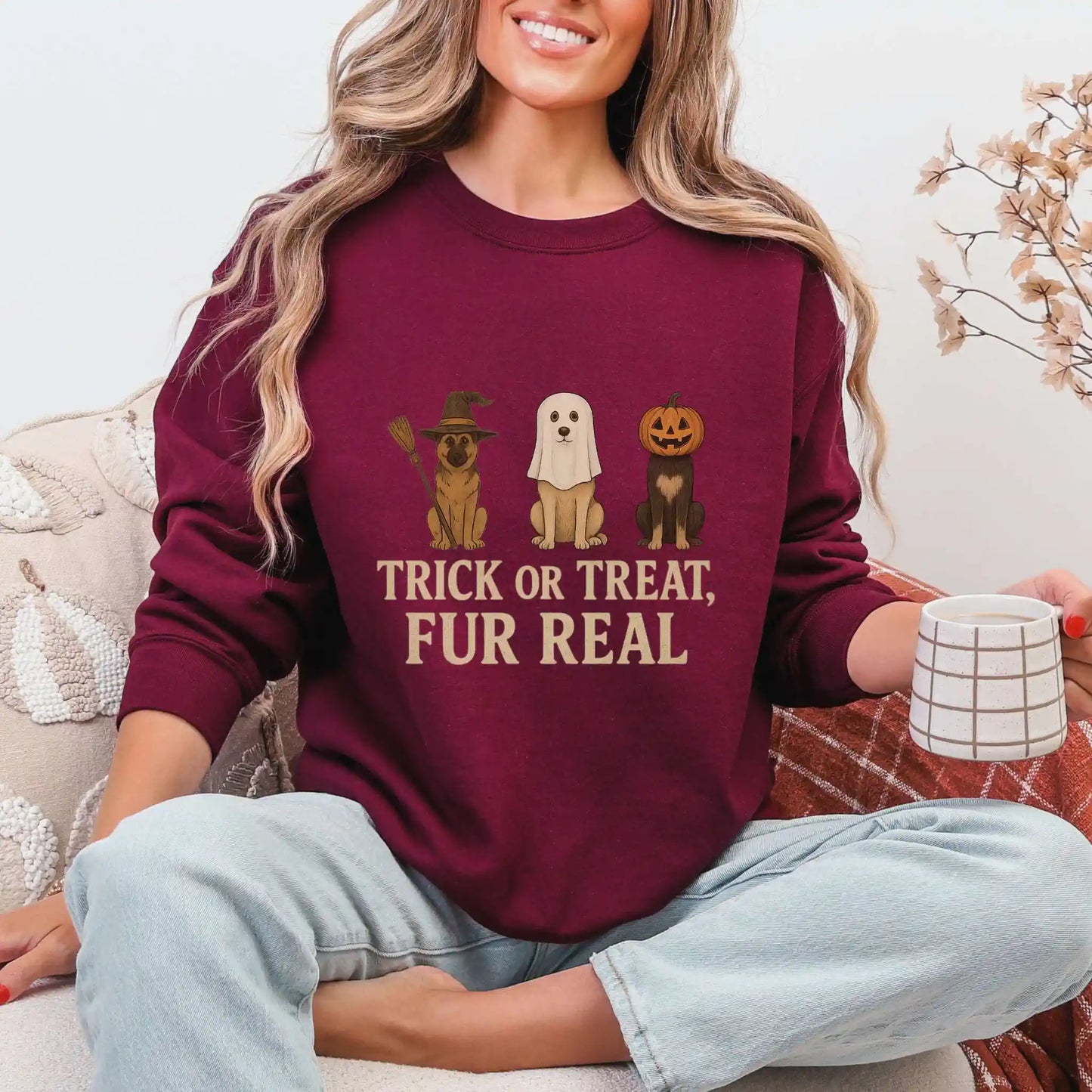 Woman wearing a maroon sweatshirt with Halloween-themed dog graphics and "Trick or Treat, Fur Real" text, sitting on a couch.