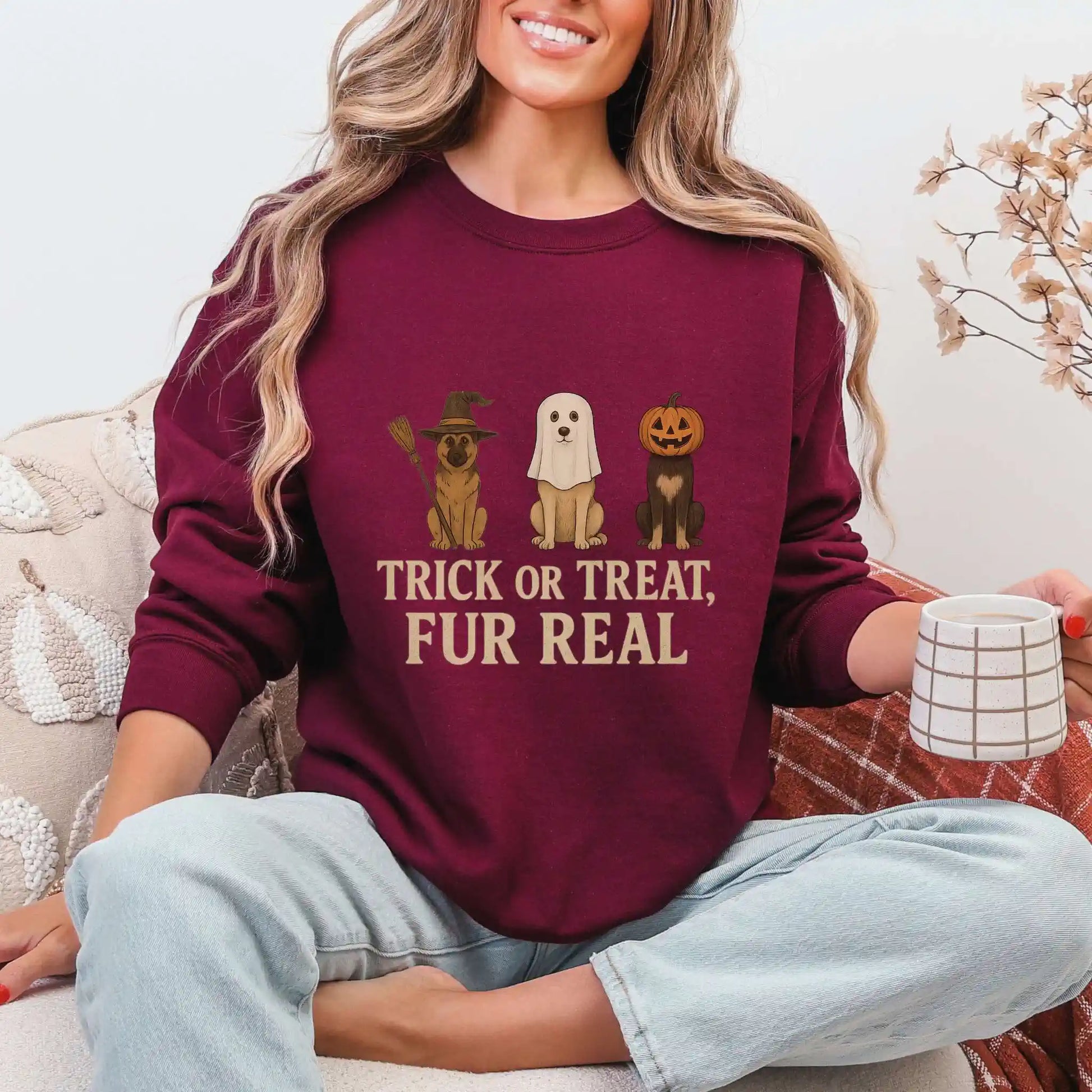 Woman wearing a maroon sweatshirt with Halloween-themed dog graphics and "Trick or Treat, Fur Real" text, sitting on a couch.