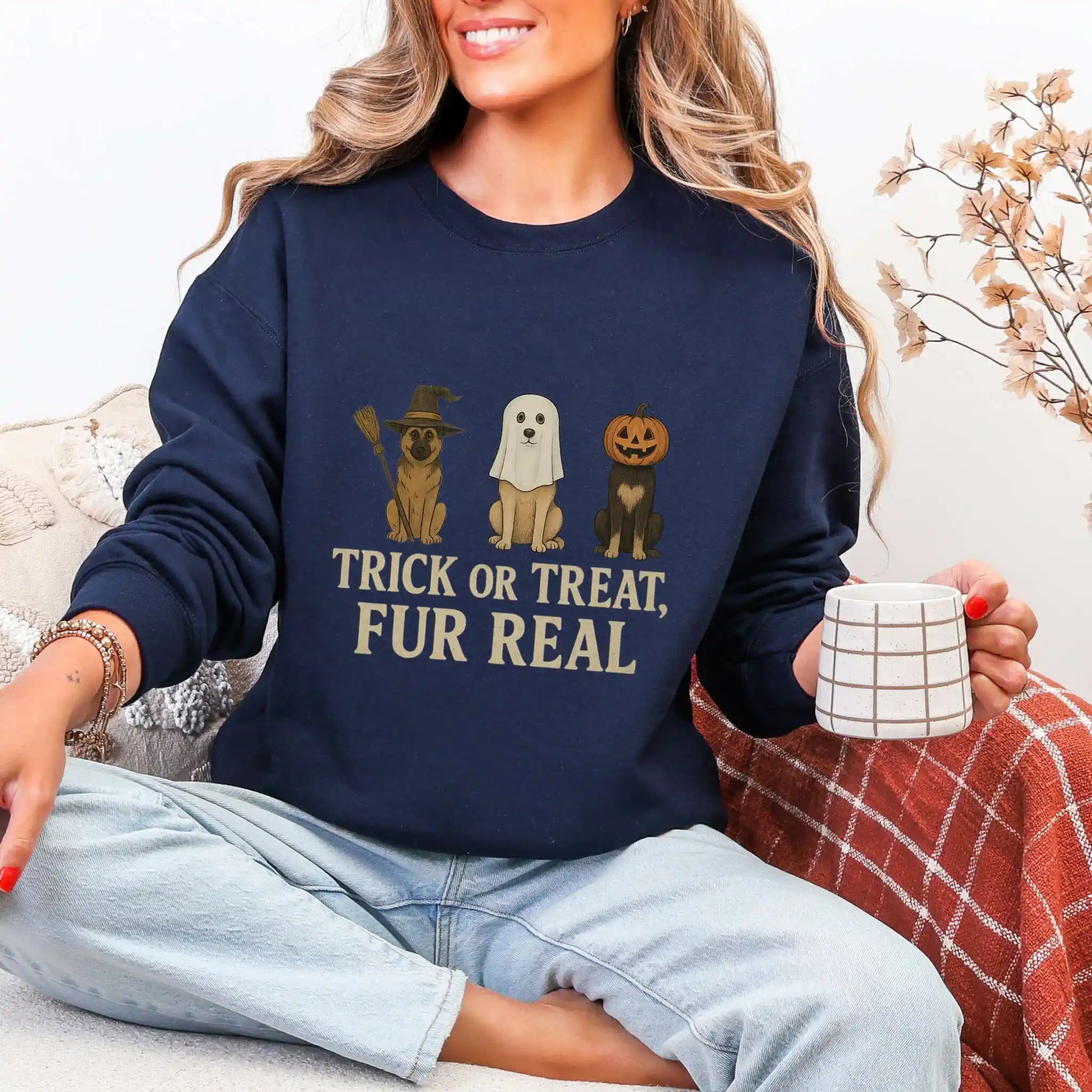 Woman wearing a navy sweatshirt with Halloween-themed dog graphics and "trick or treat, fur real" text, sitting on a couch.