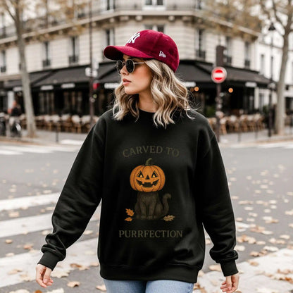 A woman wearing a black sweatshirt with a Halloween design of a cat with a pumpkin head and text 'Carved to Purrfection', standing on a street.