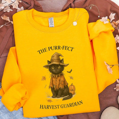 Yellow sweatshirt with a black cat in a scarecrow outfit design, with "The Purr-fect Harvest Guardian" text, lying on a brown jacket background.