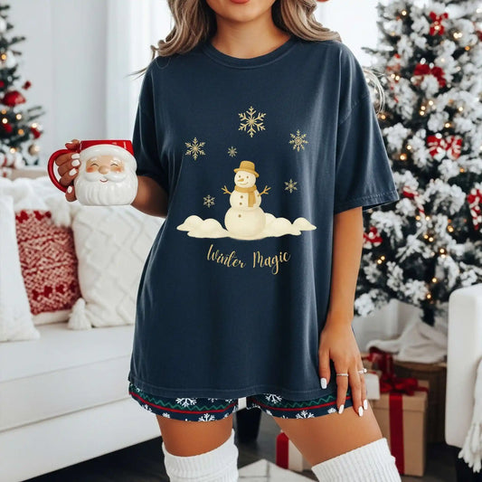 A woman wearing a navy blue t-shirt with a snowman design and 'Winter Magic' text, holding a Santa mug in a festive room.