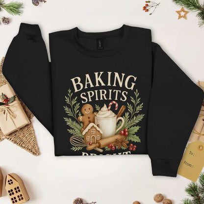 Black colored Beacon & Bramble Christmas sweatshirt featuring the phrase ‘Baking Spirits Bright’ above a festive design with a gingerbread man, mug of cocoa topped with whipped cream and a candy cane, cinnamon sticks, greenery, and holly berries. Surrounded by cozy holiday decor and greenery accents.