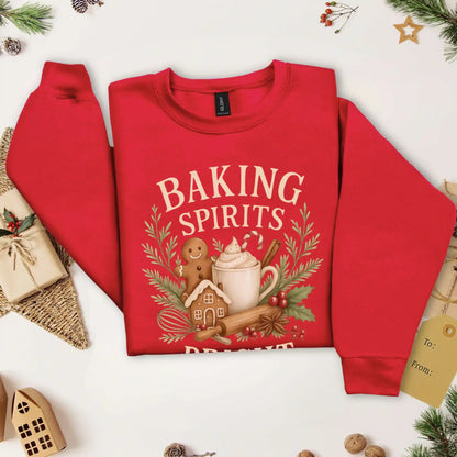 Cardinal red-colored Beacon & Bramble Christmas sweatshirt featuring the phrase ‘Baking Spirits Bright’ above a festive design with a gingerbread man, mug of cocoa topped with whipped cream and a candy cane, cinnamon sticks, greenery, and holly berries. Surrounded by cozy holiday decor and greenery accents.