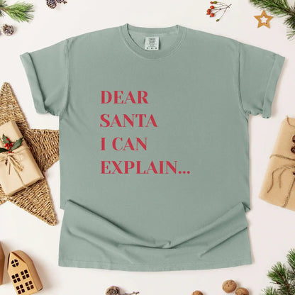 Green t-shirt with 'Dear Santa I can explain' text on a festive background with presents and decorations.