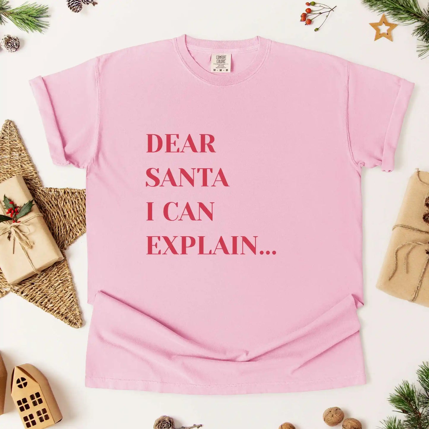 Pink t-shirt with 'Dear Santa I can explain' text on a white background with Christmas decorations.