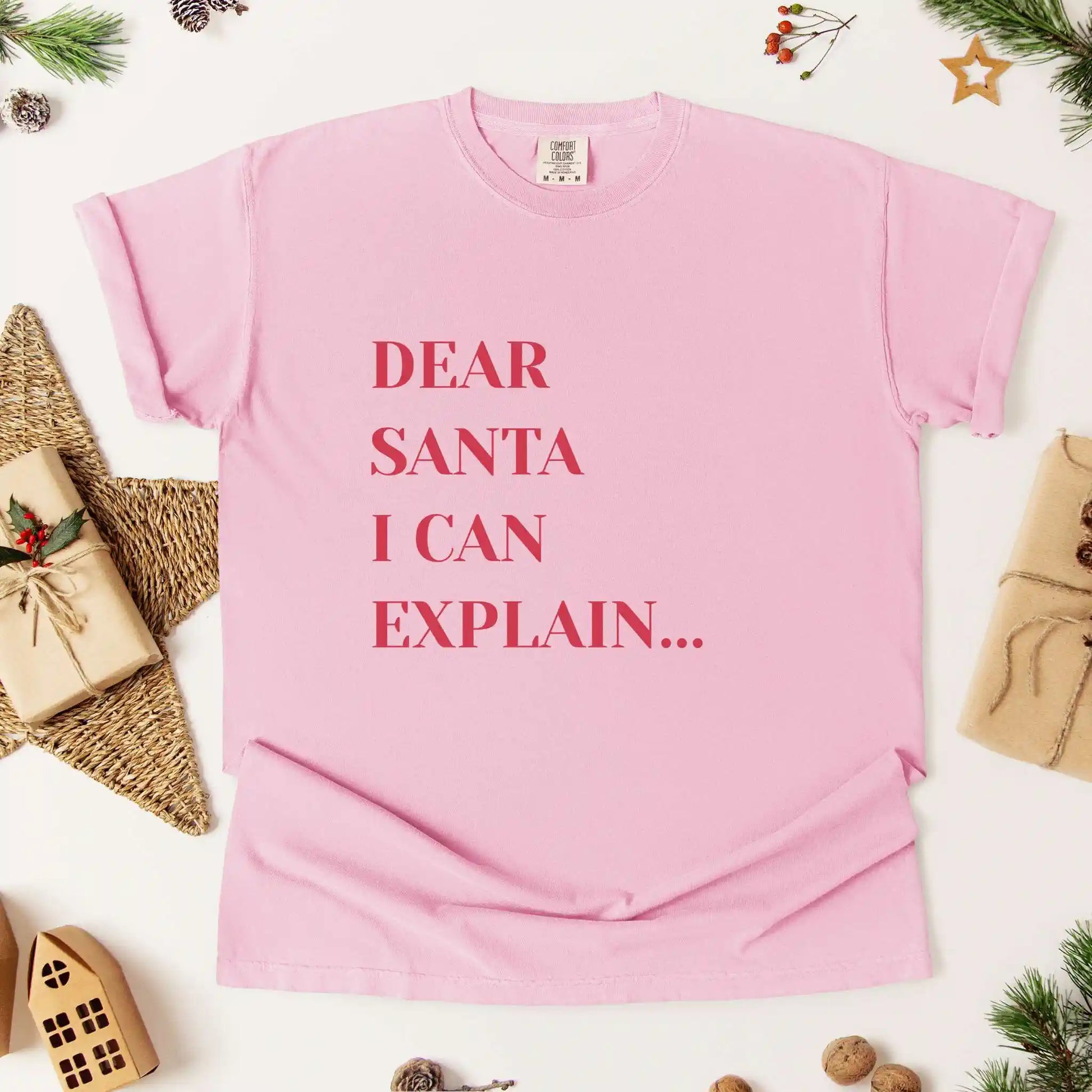 Pink t-shirt with 'Dear Santa I can explain' text on a white background with Christmas decorations.