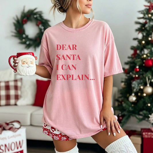 Person wearing a pink t-shirt with 'Dear Santa I can explain' text in a festive room.
