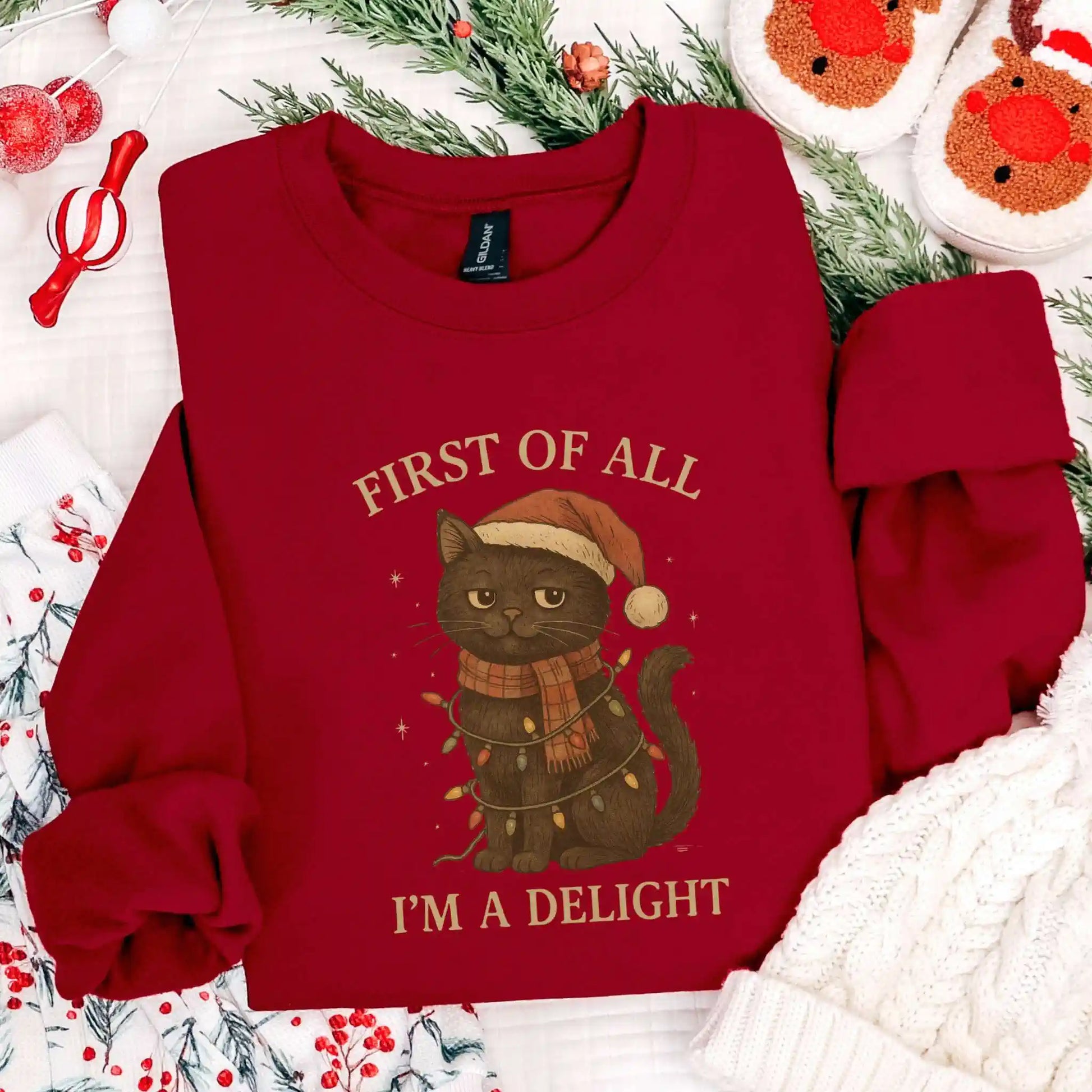 Red sweatshirt with a cat christmas-themed graphic and "First of all I'm a delight" text on a festive background