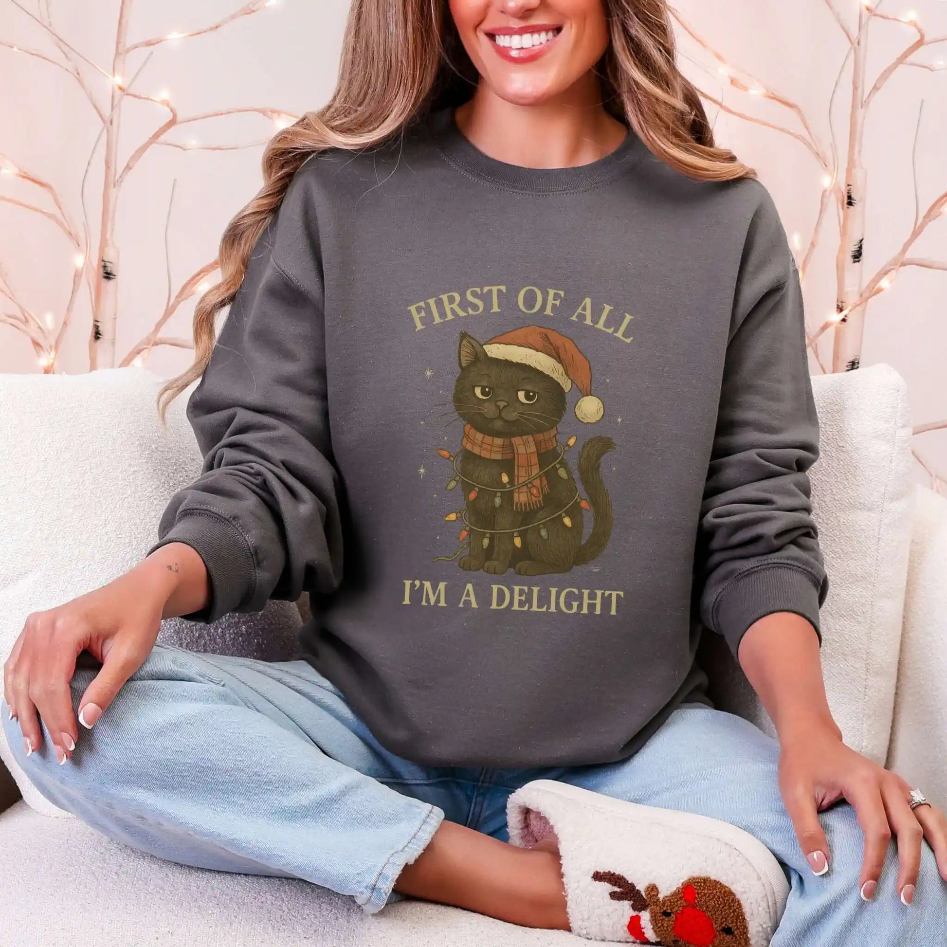 Person wearing a charcoal sweatshirt with a Christmas-themed cat design, sitting on a white couch.