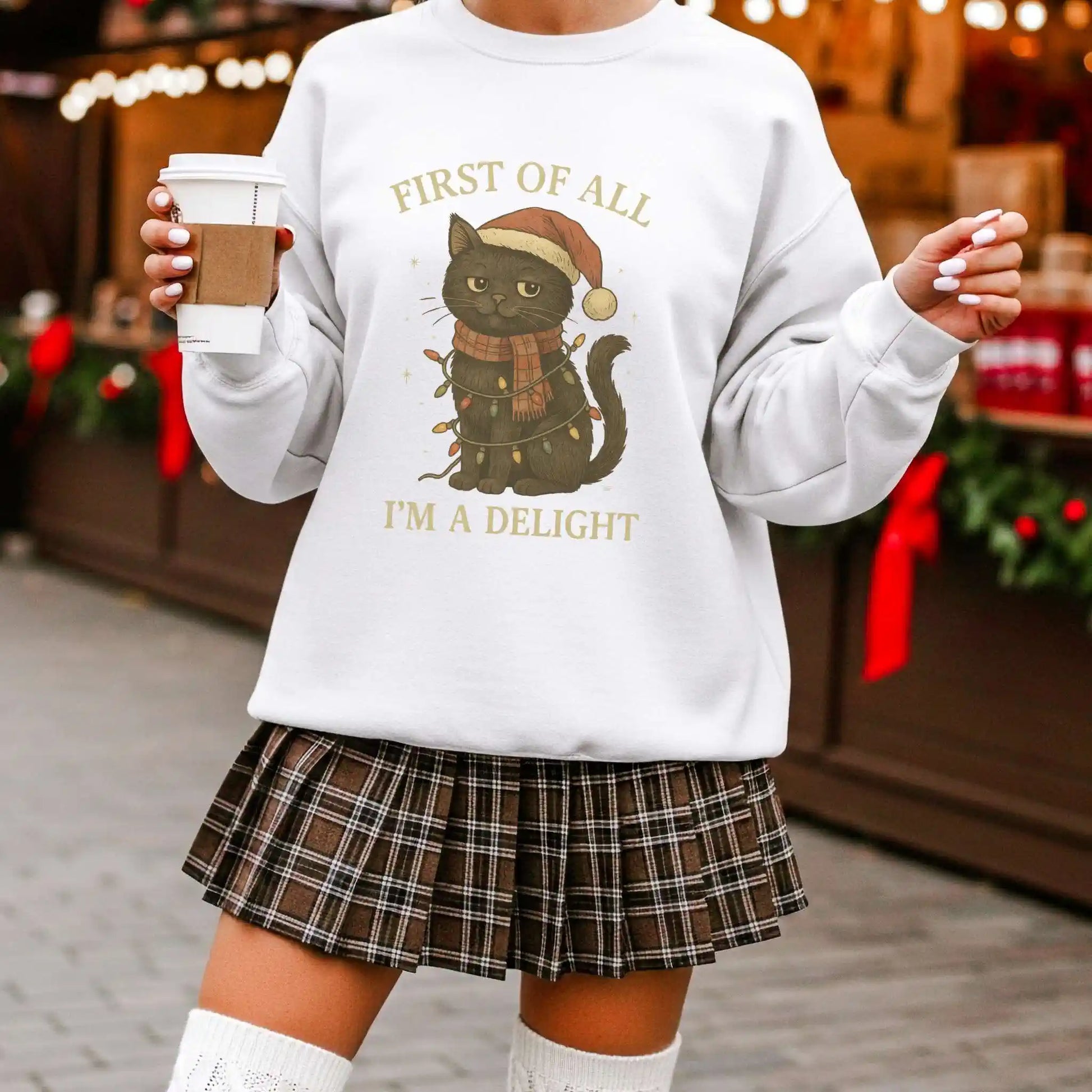 Person wearing a white sweatshirt with a Christmas-themed cat graphic and text, holding a coffee cup.