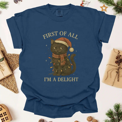 Christmas cat graphic t-shirt by Beacon & Bramble featuring a black cat in a Santa hat and scarf wrapped in holiday lights with the phrase ‘First of all, I’m a delight.’ Cozy vintage holiday design on a navy blue tee.