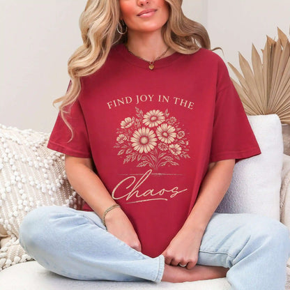 Woman wearing a Chili colored t-shirt with floral design and "Find joy in the chaos" text, sitting on a couch.