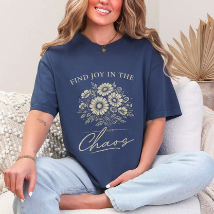 Woman wearing a Navy colored t-shirt with floral design and "Find joy in the chaos" text, sitting on a couch.